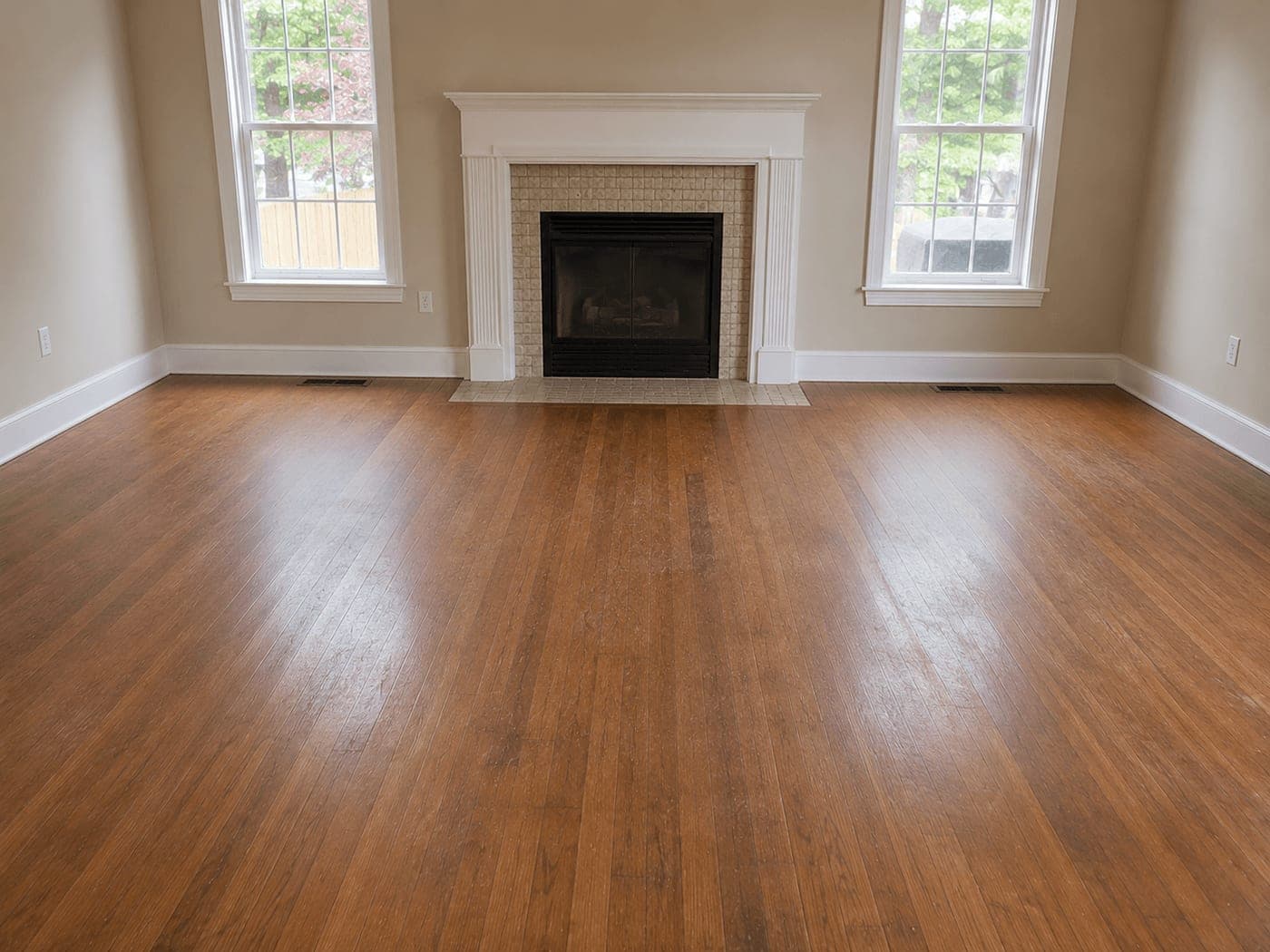 Living room with a fireplace and worn hardwood floor before restoration